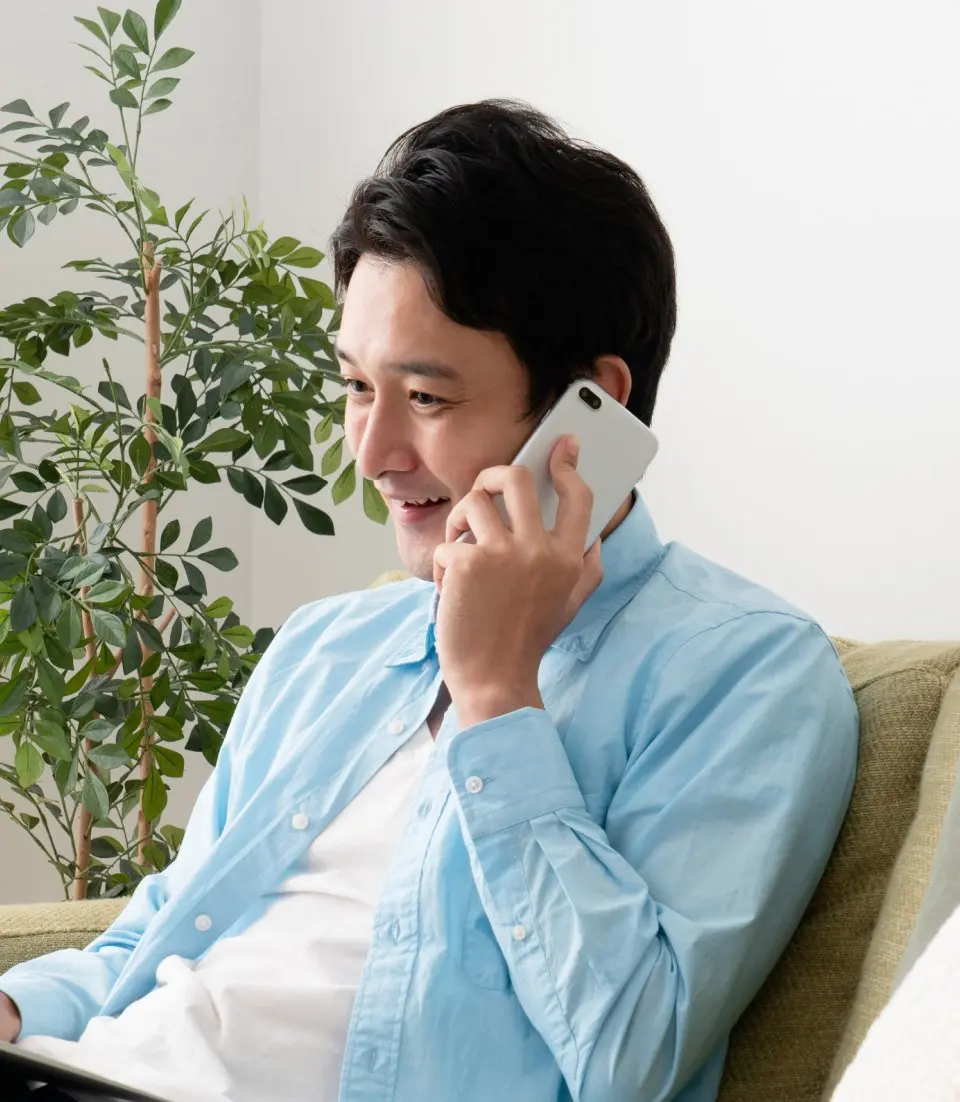 ソファに座り、スマートフォンで通話している男性。