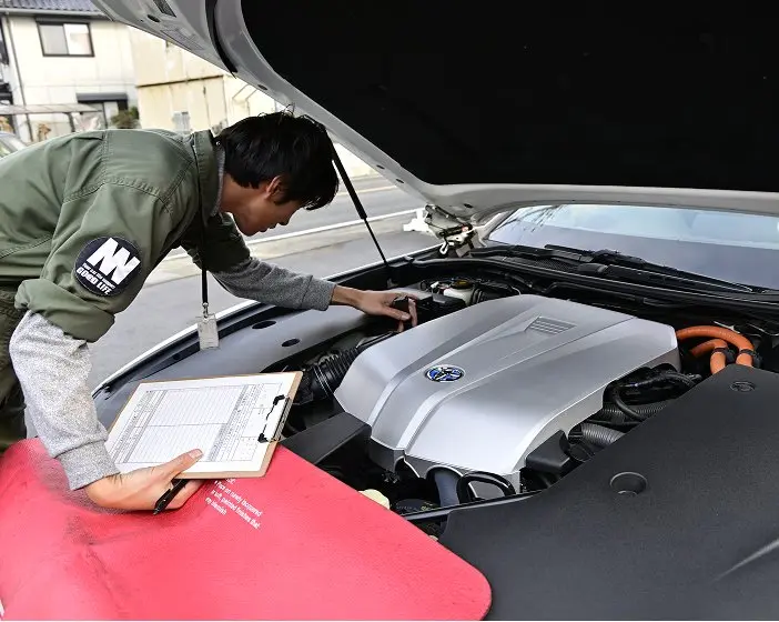 車のボンネットを開けてエンジンを点検している整備士。