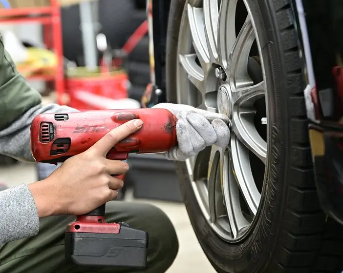 電動工具を使って車のタイヤを取り外している整備士の手元。