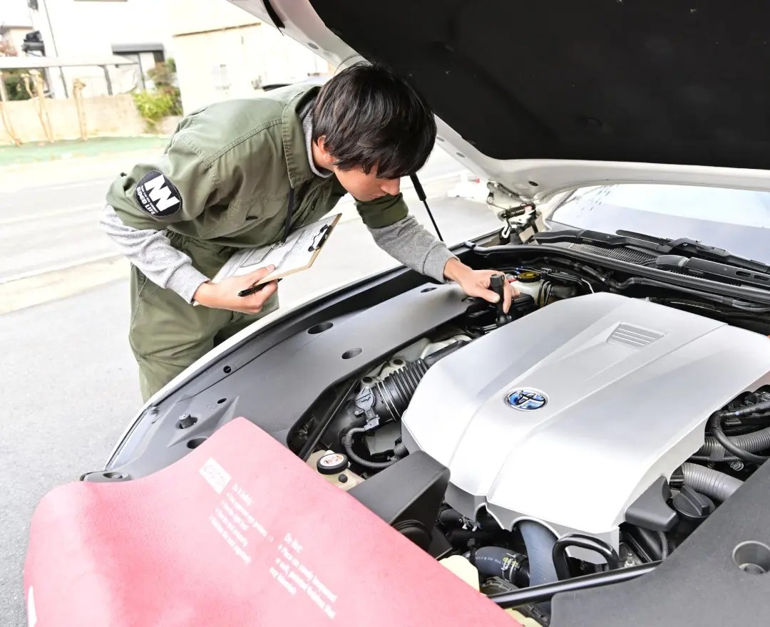 車のエンジンルームを点検する整備士