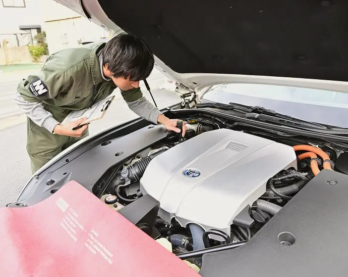  車のボンネットを開けてエンジンを点検している整備士。