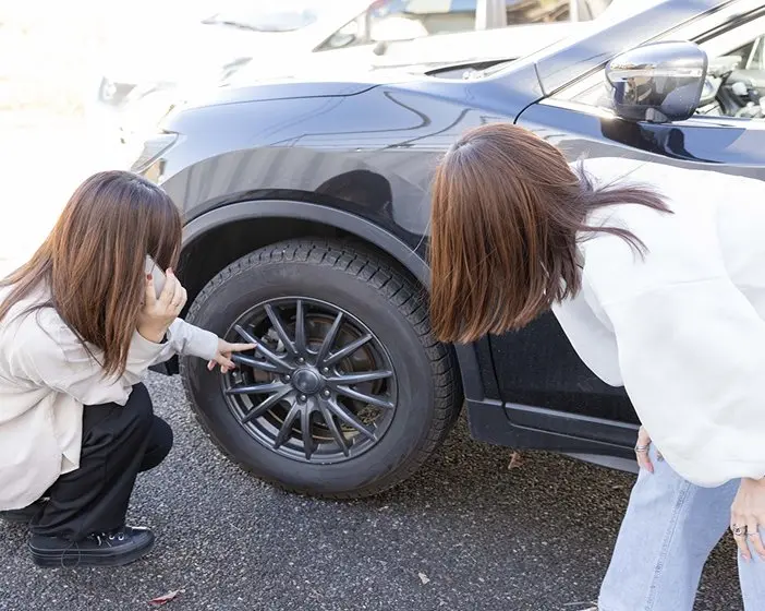 車のタイヤを指差して確認している2人の女性。