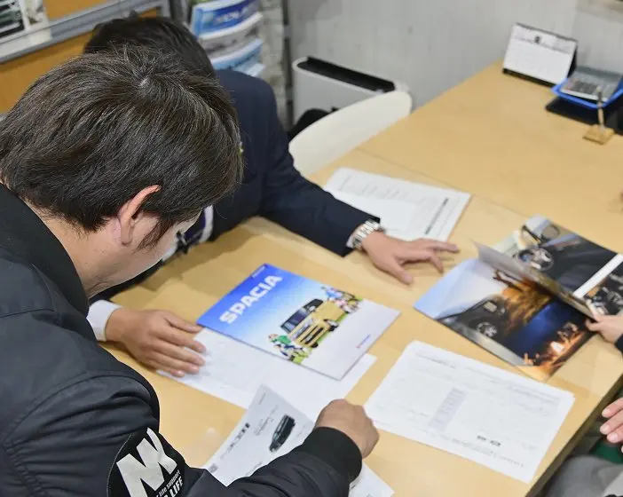 テーブルを囲んで車のカタログを見ながら話し合う人々。