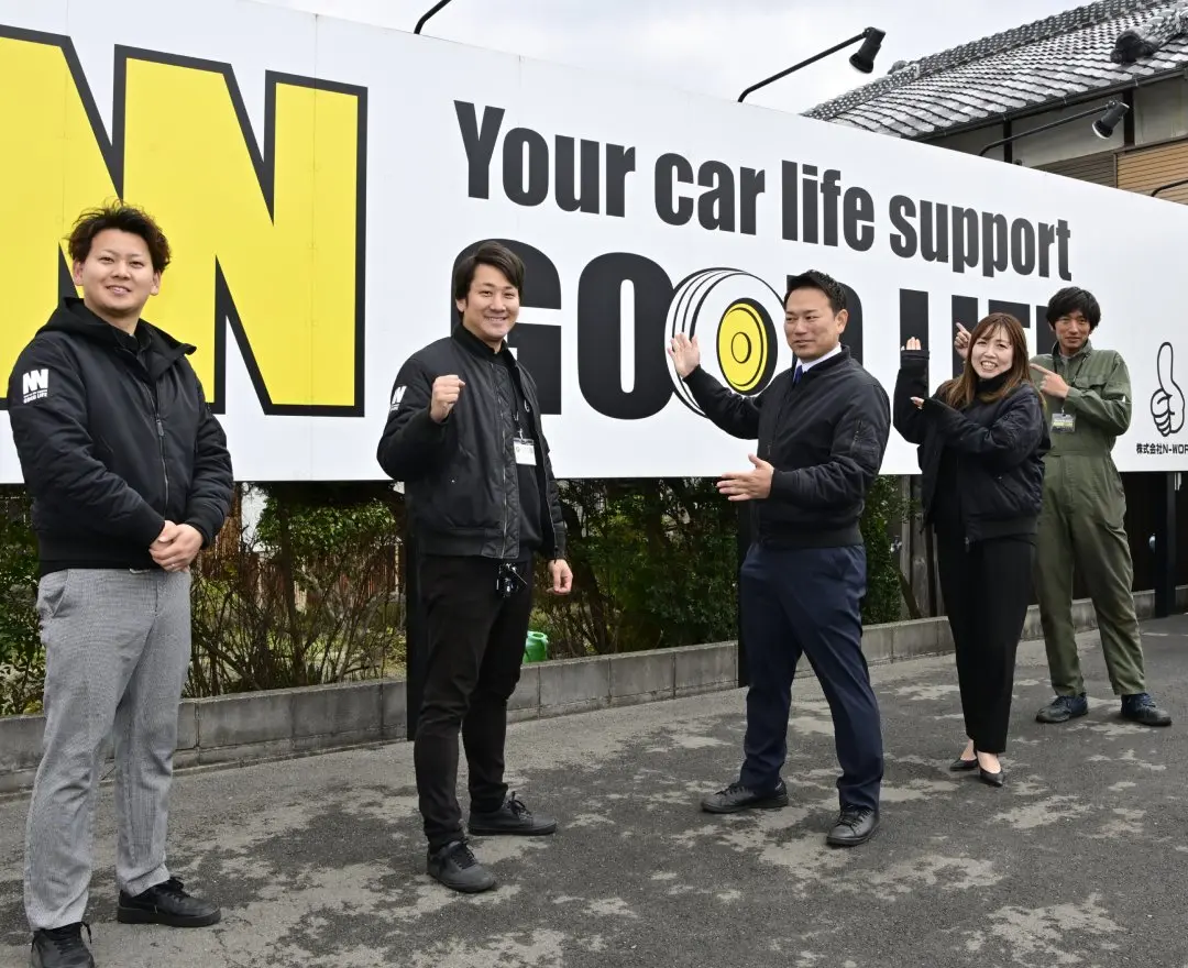 会社の看板の前に立つスタッフたち